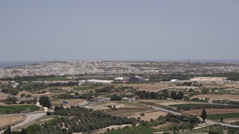 Paisaje-Rural-De-4k-Con-El-Mar-Mediterráneo-Y-Un-Pequeño-Pueblo-A-Lo-Lejos-En-La-Isla-De-Malta-Durante-Un-Caluroso-Día-De-Verano