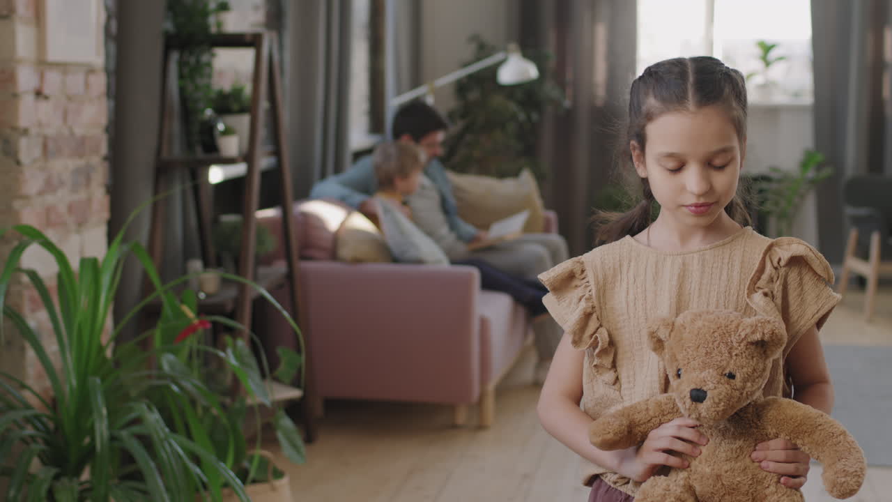 A girl holding a teddy bear with her family in the background
