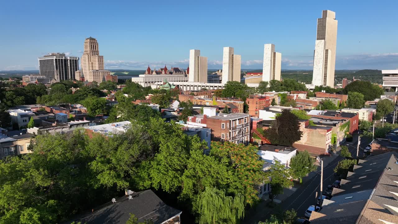 Row homes and two-story houses in red brick style in front of downtown skyline. Sunny day with blue sky in Albany, New York. Aerial wide shot. New York State capitol and Empire State plaza in back
