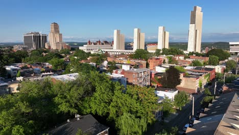 row homes and two-story houses in red brick style in front of downtown skyline. sunny day with blue sky in albany, new york. aerial wide shot. new york state capitol and empire state plaza in back