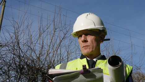 portrait of an architect building inspector inspecting a construction site with a clip board and architectural plans