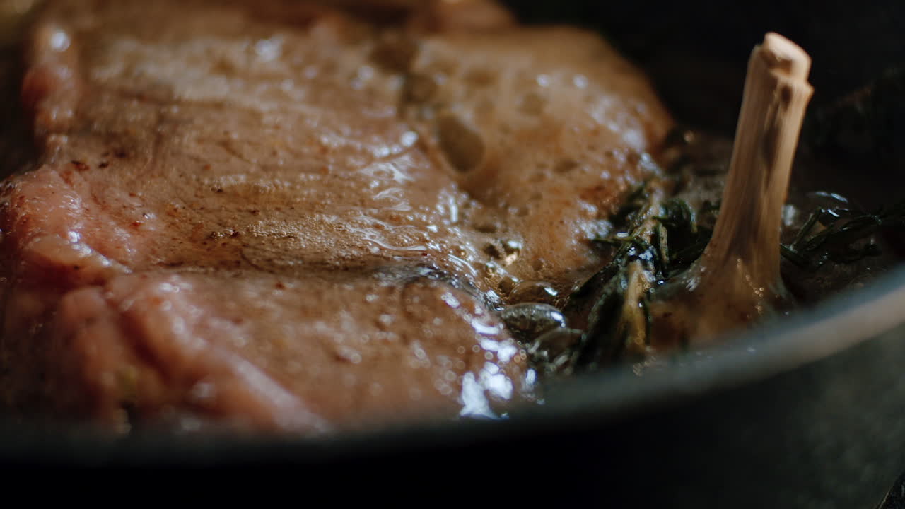 Man is putting melted sizzling butter on piece of meat in hot iron pan, close up