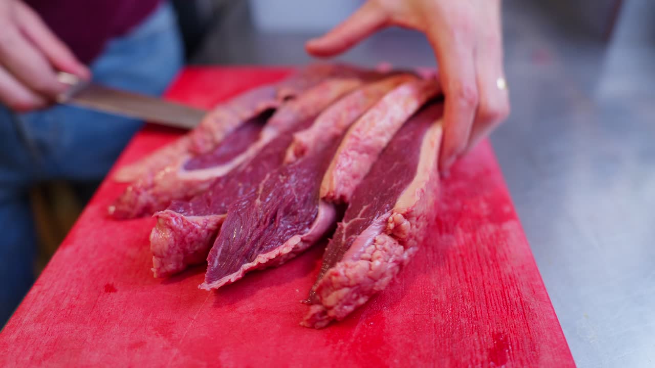 Primo piano di uno chef che affetta manzo crudo su un tagliere rosso