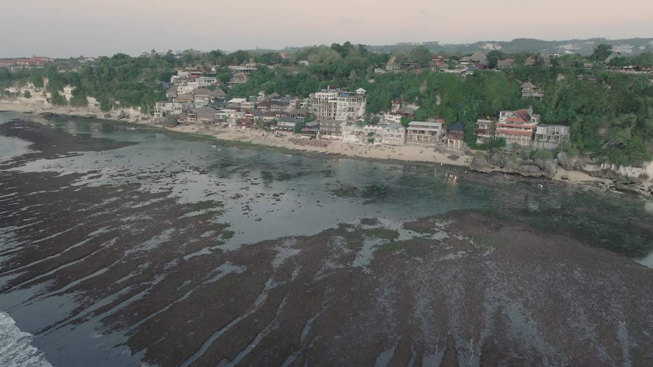 Far away Panning Drone shot of Bingin Beach buildings at sunset and low tide in Uluwatu Bali Indonesia