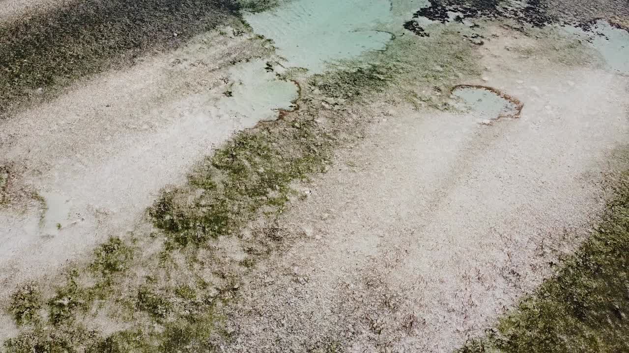 Aerial reversing flying over crystal clear ocean at low tide with sand patterns on tropical island of Timor-Leste, Southeast Asia