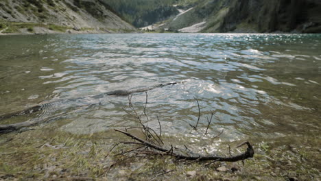 a shot of the edge of lake, water waving, branch in the water in background is valley and mountains