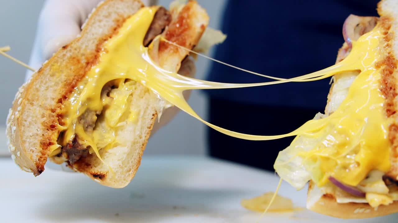 Appetizing hamburger with melted cheese. Chef holds ready juicy cheeseburger cut in halves. Hot delicious fast food. Close-up