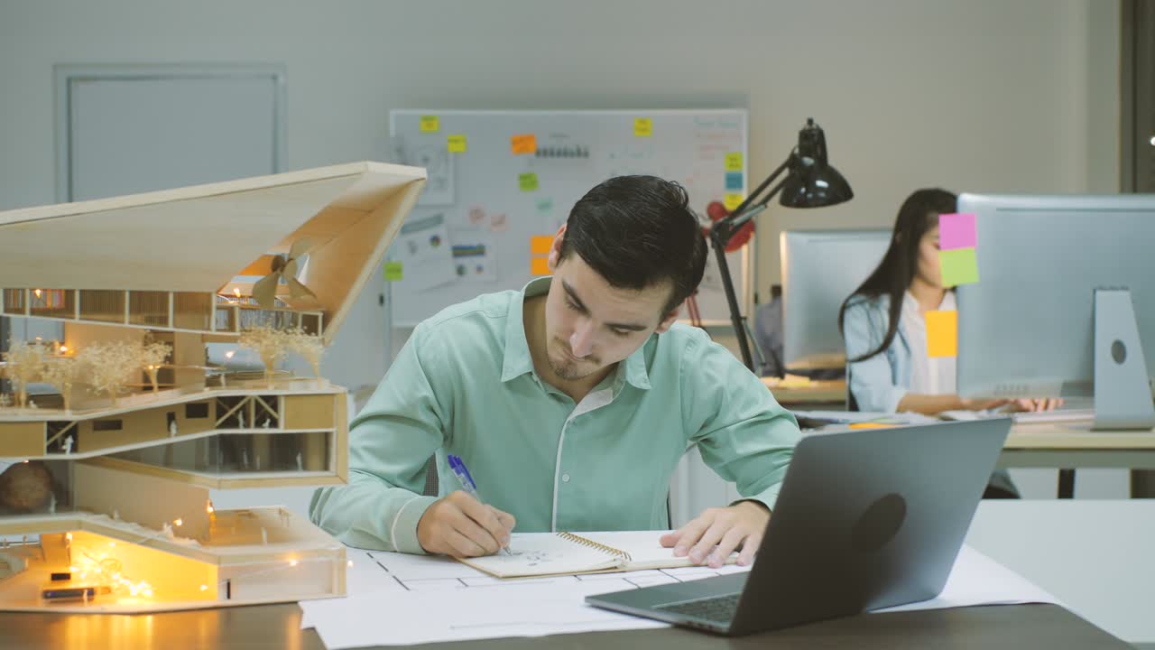 joven arquitecto caucásico confiado trabajando en un modelo arquitectónico en la oficina por la noche