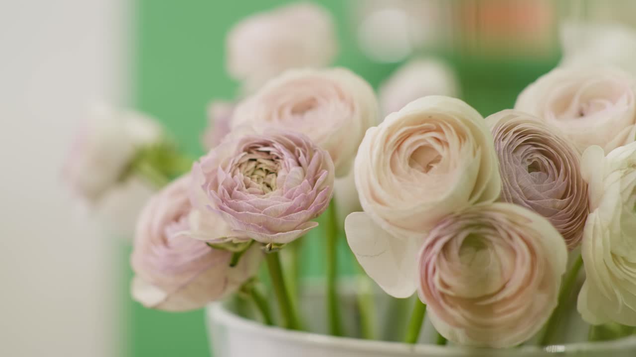 A smooth left-to-right dolly shot glides past an elegant bouquet of blush and white Ranunculus flowers, maintaining a crisp, fixed focus on the delicate petals