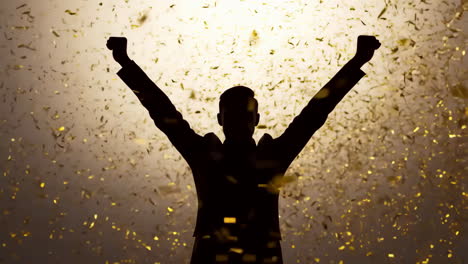 silhouette of a person celebrating with arms raised amidst a shower of golden confetti