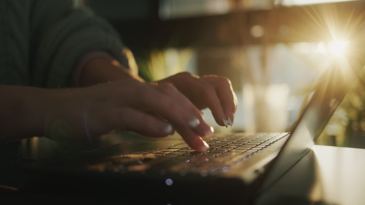 manos femeninas en el teclado de la computadora portátil escribiendo texto. el sol de la ventana ilumina hermosamente los dedos y teclado