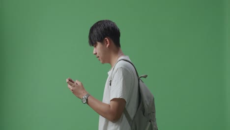 vista lateral de un estudiante asiático emocionado jugando a un juego móvil mientras camina en el estudio de pantalla verde