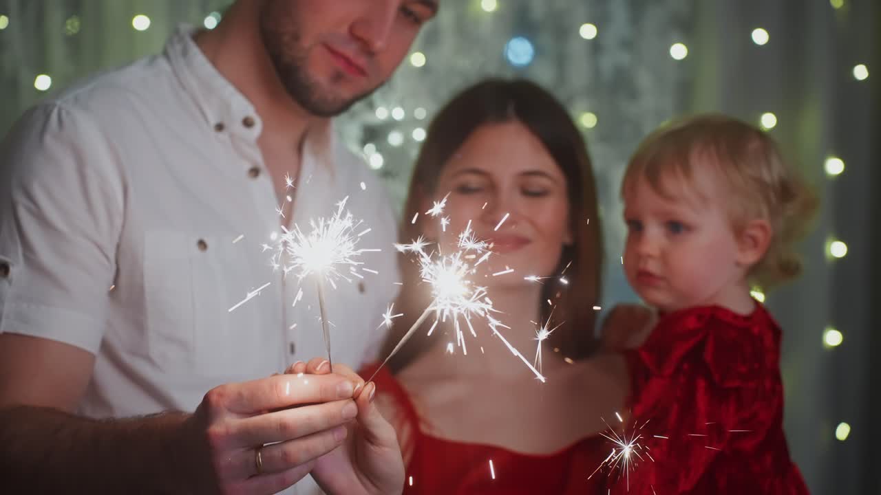 Joyful family moment capturing parents and child holding sparklers, standing near decorated Christmas tree, radiating warmth and festive happiness during winter holiday celebration