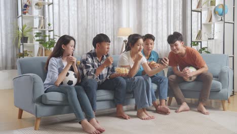 asian teenagers cheering and watching football game on smart phone and disappointed at home