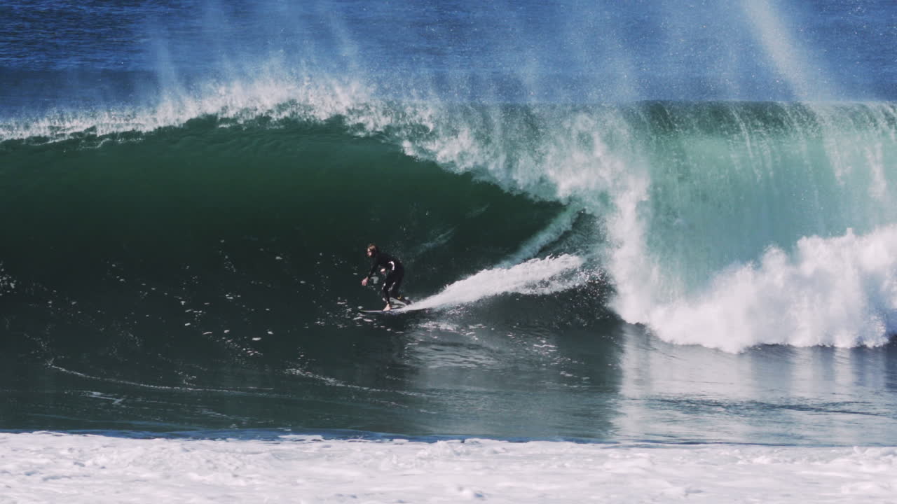 Aerial tracking of smooth green barrel as surfer crouches inside mid-section