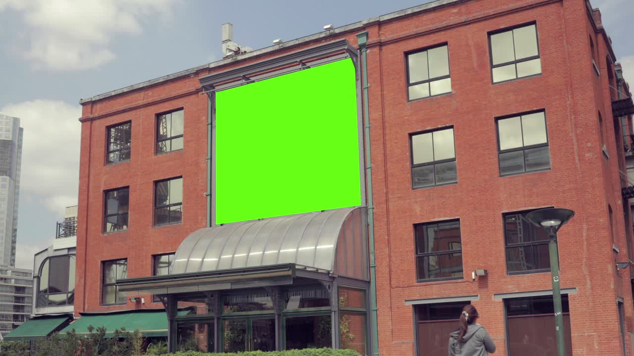 Green screen-billboard på en murstensbygning med en fodgænger.
