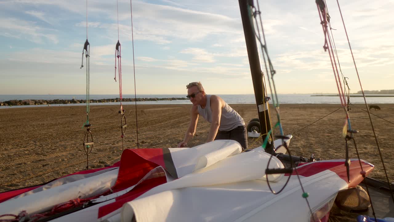 hombre preparando las velas de un catamarán en la playa por la mañana
