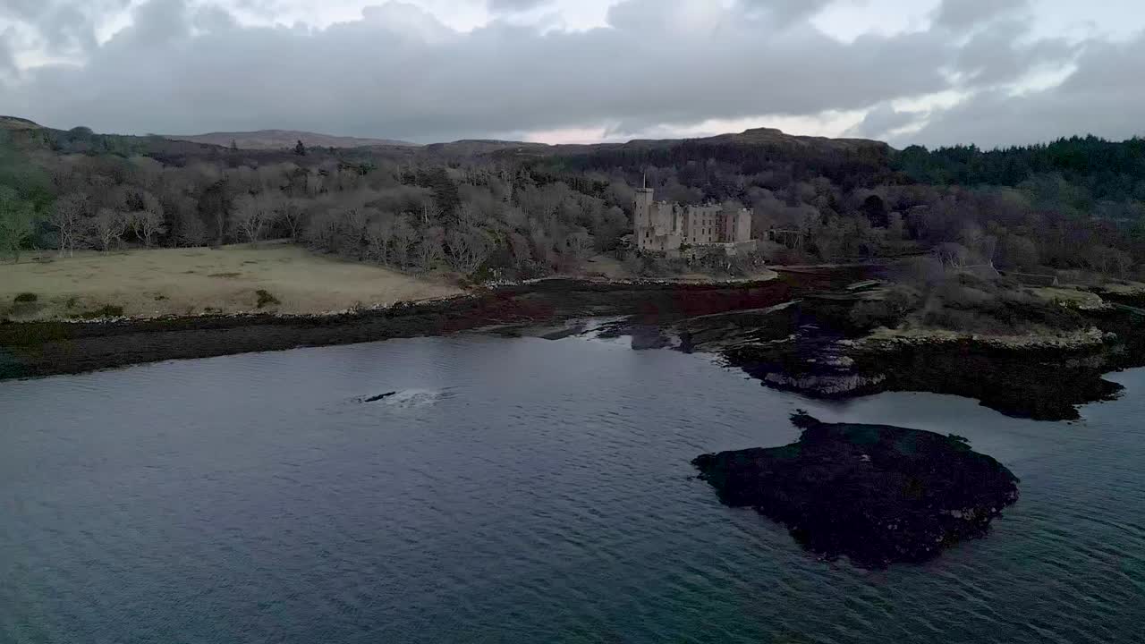 el castillo de dunvegan en la isla de skye, rodeado de bosques y aguas costeras al anochecer, vista aérea