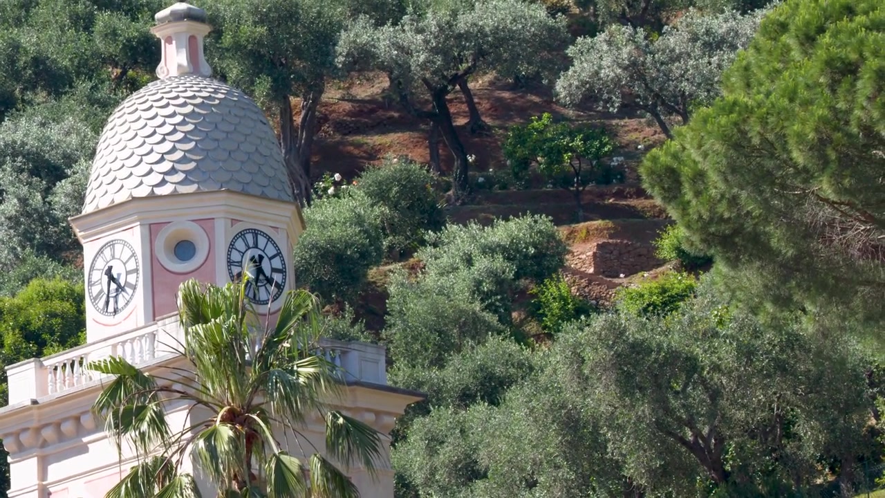 Un alejamiento lento revela una torre de reloj tradicional anidada entre olivos en Portofino.