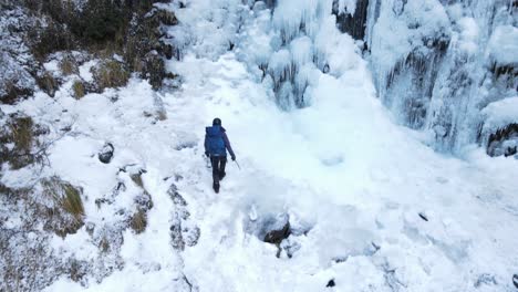 woman climber with backpack walking towards a frozen waterfall