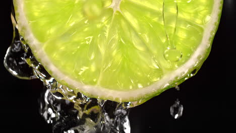 una rebanada de cal y agua salpicando sobre el fondo negro en cámara lenta