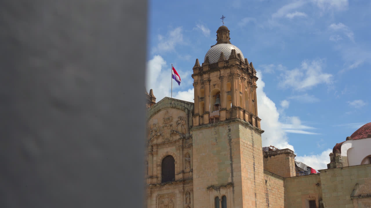 Reveal establishes Oaxaca cathedral towers rising above city rooftops in warm daylight