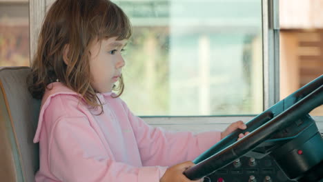 active toddler girl turns steering wheel of old bus and beeping while sitting in driver's seat