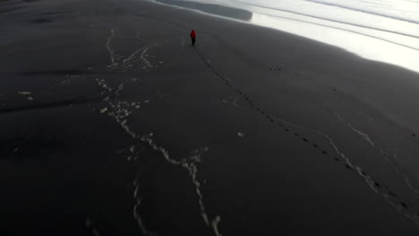 drone footage of man on stokkness beach panning up towards dramatic mountains on the coast of southern iceland