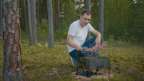 adult man is grilling sausages in forest picnic at nature at summer weekend or vacation resting and relax