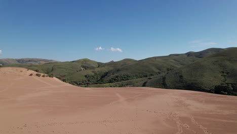 Serene-sand-dune-ridge-line-dotted-with-foot-steps-and-car-tracks-below-arid-mountainside