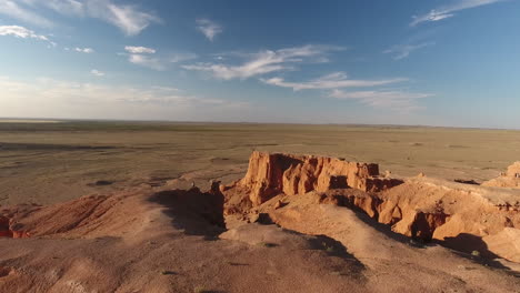 man standing on the edge of flaming cliffs bayanzag aerial drone shot mongolia