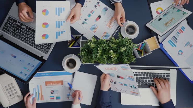 Draufsicht auf ein Team, das Finanzunterlagen austauscht und Managementstatistiken bespricht