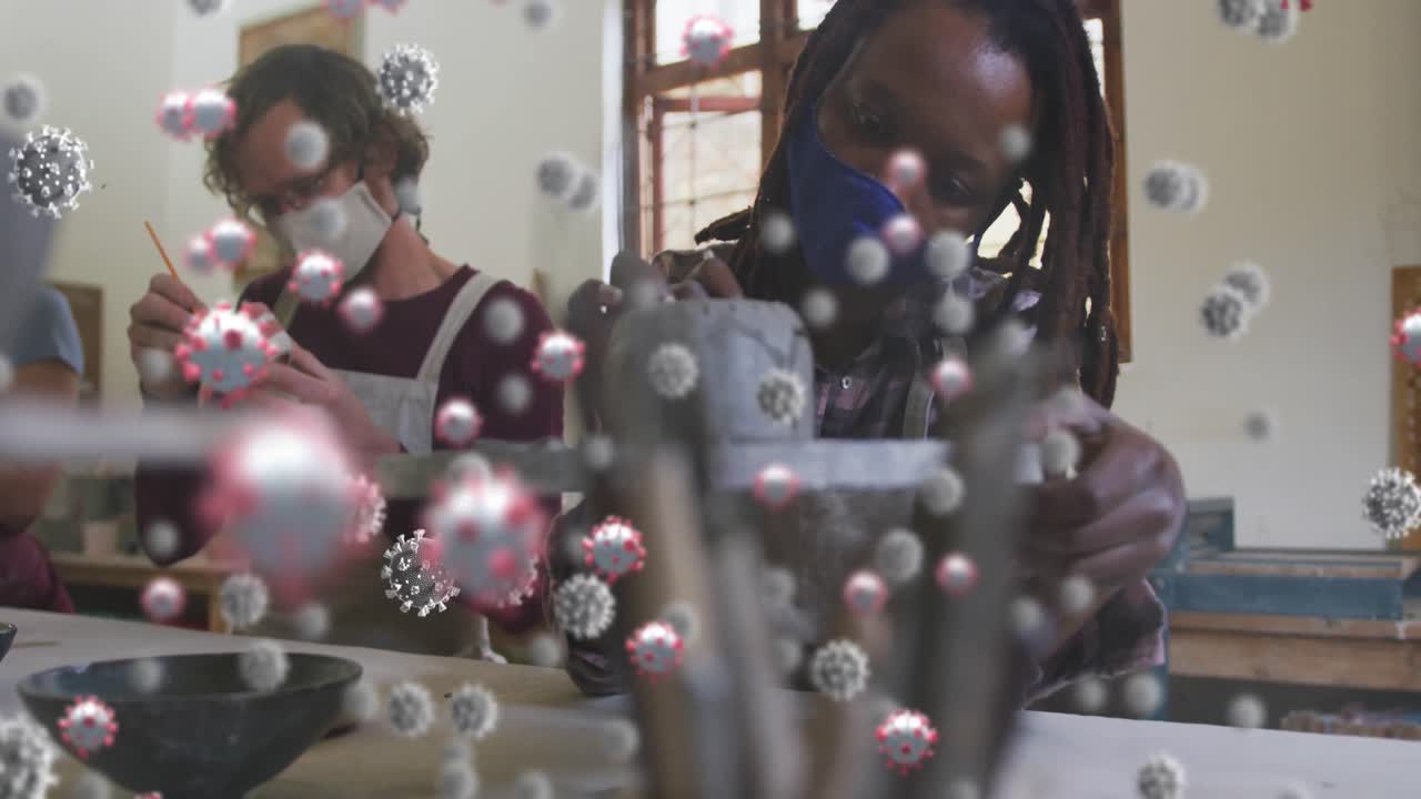 Animation of virus cells over diverse workers with face masks painting pottery