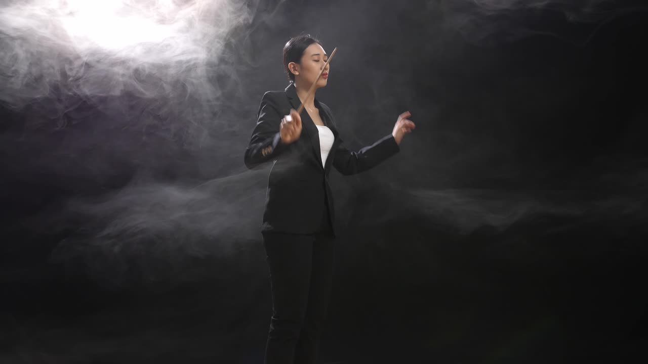 vista lateral de una mujer conductora asiática sosteniendo un bastón y mostrando un gesto rápidamente en el estudio negro con niebla