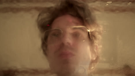 man's face reflected through blurry glass