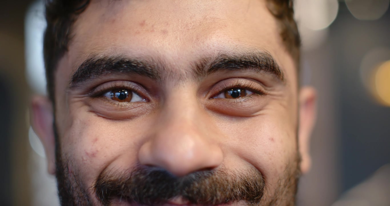 Hombre manteniendo contacto visual con la cámara, parpadeando y sonriendo gradualmente para un retrato de estudio con efecto bokeh.