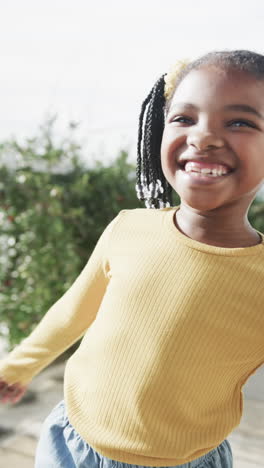 vertical video of portrait of happy african american girl smiling on sunny terrace, slow motion