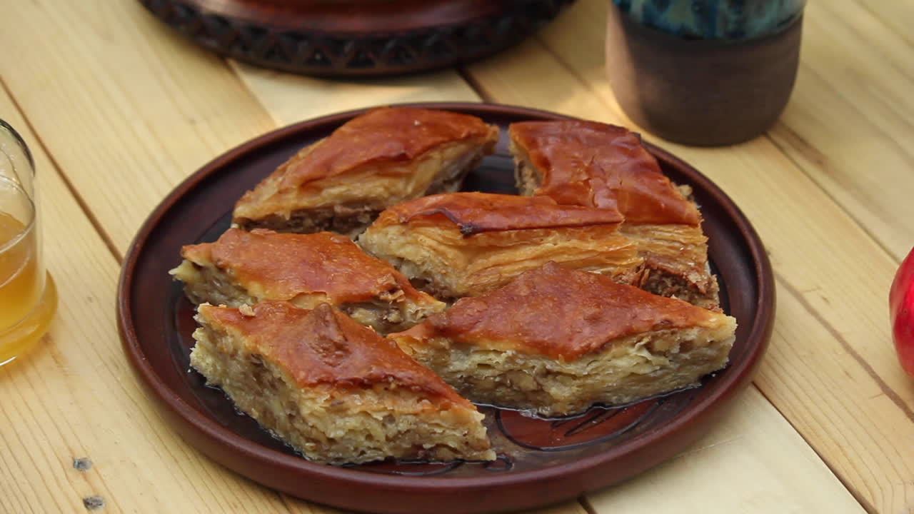 Prato cheio de baklava na mesa ao lado de uma romã vermelha.