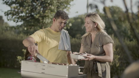 smiling man putting mushrooms and shashlik on plate of his wife