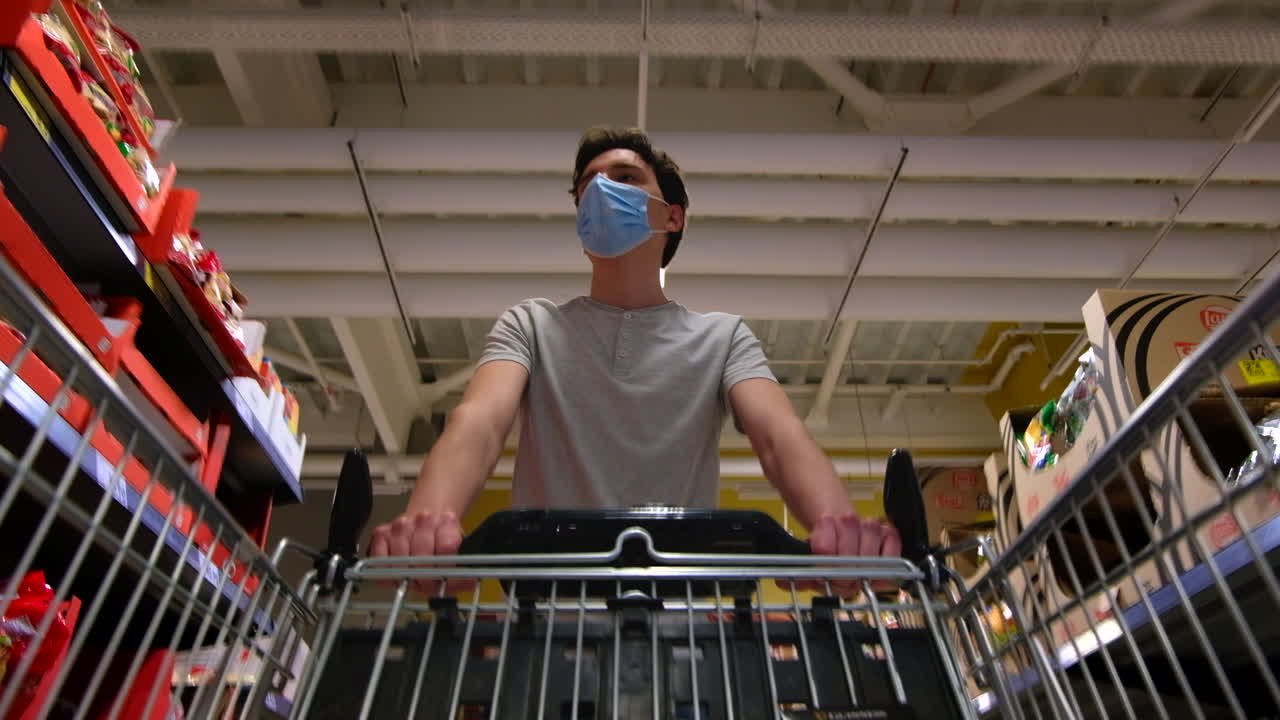 CHISINAU, MOLDOVA - JUNE 5, 2020: Young man with a protective medical mask walking in a supermarket and looking around. View from the cart. Corona Virus idea