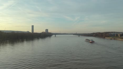 Filmische-Drone---Luftaufnahme-Eines-Schiffes-Auf-Dem-Rhein-In-Bonn-Mit-Dem-Posttower,-Dem-Kameha-Grand-Hotel-Und-Der-Konrad-adenauer-brücke-Zur-Goldenen-Stunde,-30-Uhr