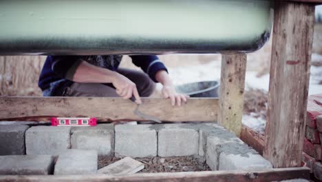 the man is using cement to fill in the gaps between the concrete blocks beneath the diy hot tub - close up