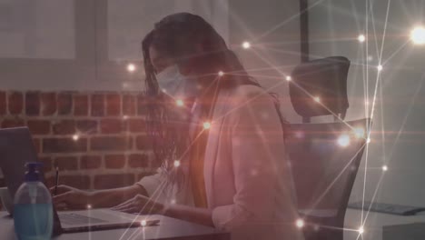 animación de una red brillante sobre una mujer de negocios con máscara facial usando una computadora portátil en la oficina