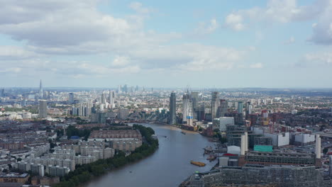 Forwards-fly-above-city.-Aerial-view-of-River-Thames-winding-in-large-town.-Cityscape-with-groups-of-tall-modern-skyscrapers.-London,-UK