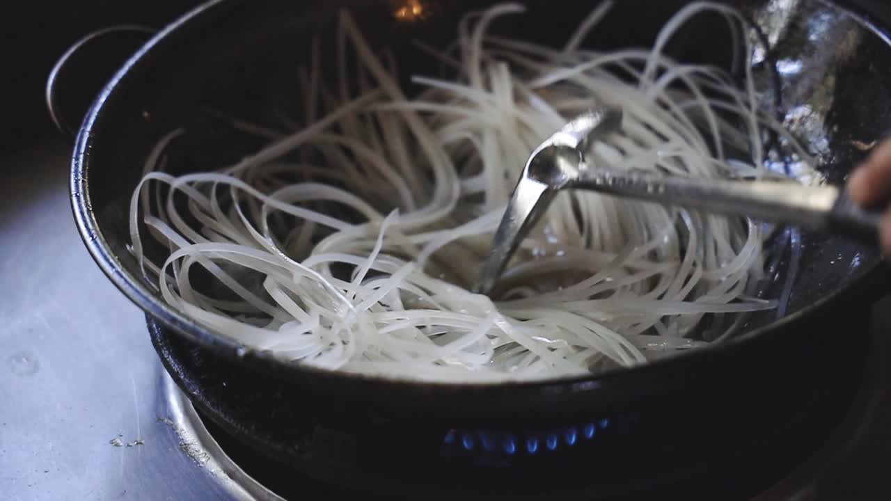 Cooking Pad Thai Series: SLO MO chef stir-frying dried rice noodles in hot pan to make Thai stir-fried noodle or Pad Thai, Thailand's signature dish.