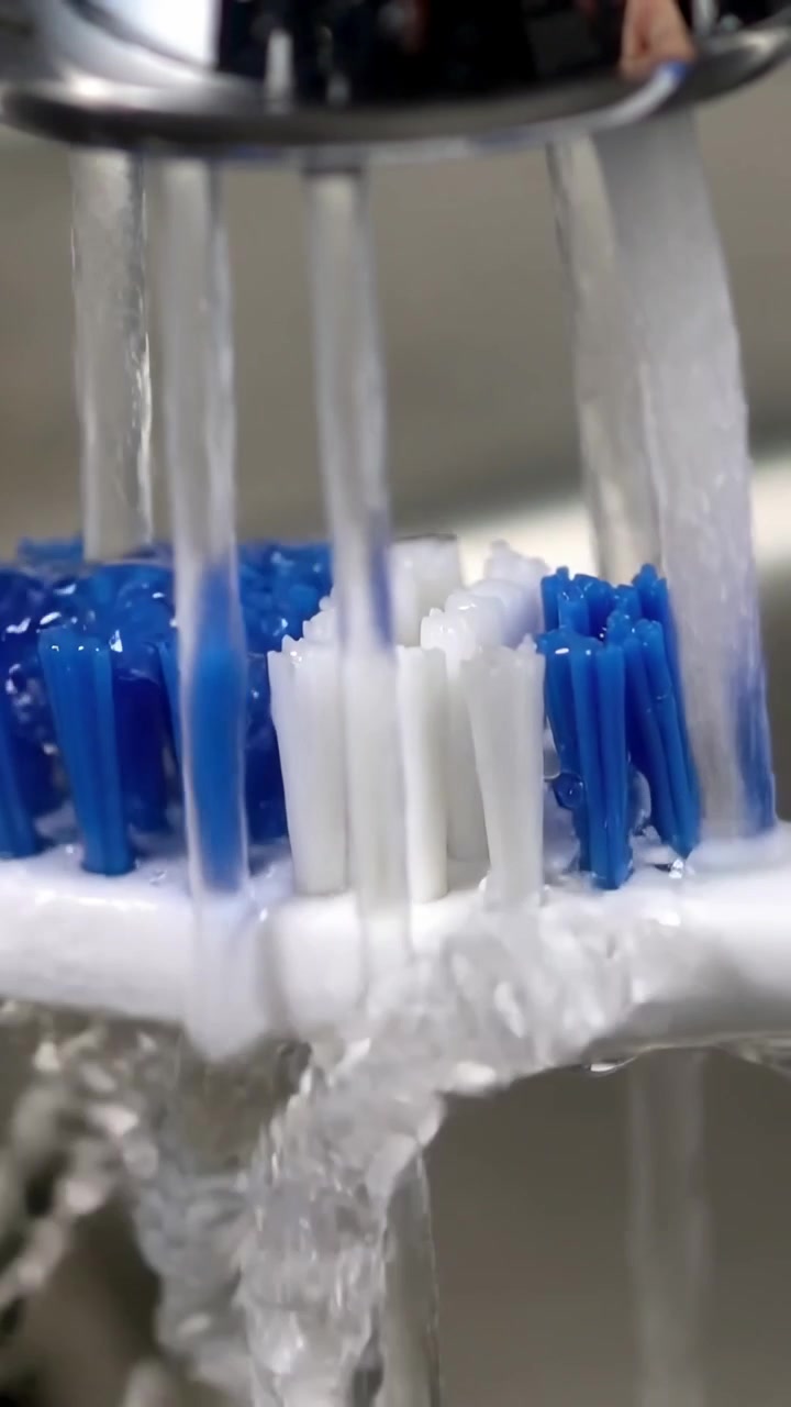 Vertical video: Running faucet rinsing detachable toothbrush head at bathroom sink, removing foam