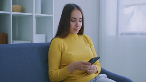 Mujer-Usando-Teléfono-Inteligente.-Chica-Guapa-Usando-La-Pantalla-Táctil-Del-Teléfono-Inteligente-Moderno-Y-Sonriendo-En-Casa