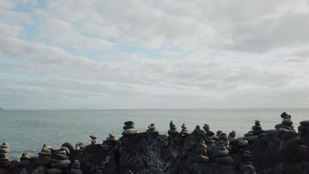 공중:호주 열대 퀸즐랜드의 바다 옆에 있는 암석 케언즈 더미 옆에서 미끄러지는 무인 항공기
