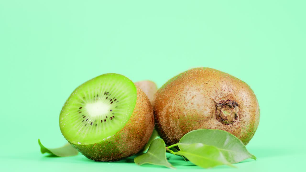 Whole and half a kiwi with leaves.