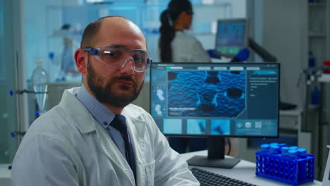 Portrait of exhausted scientist man looking at camera sitting in front of computer